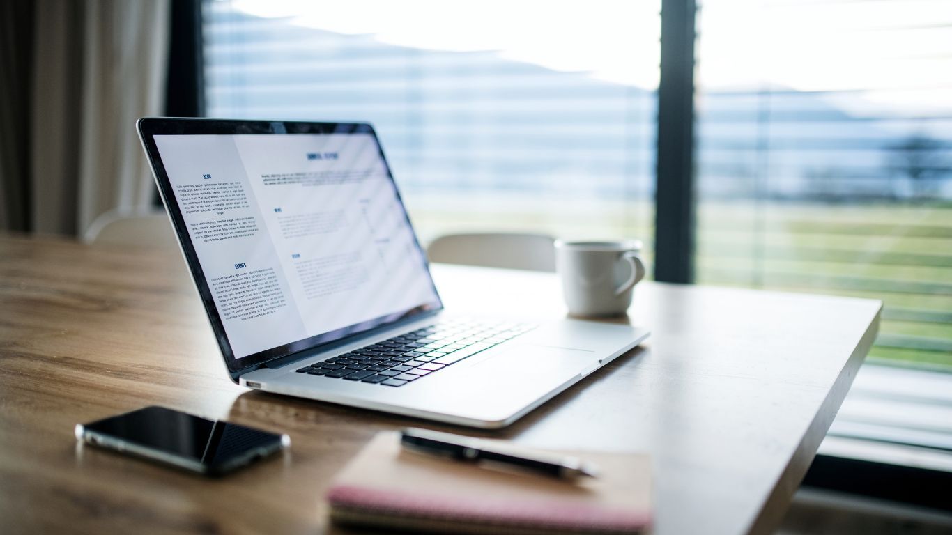 Workspace with laptop, phone, notebook, and pen representing a simple CRM workflow for contractor sales teams.