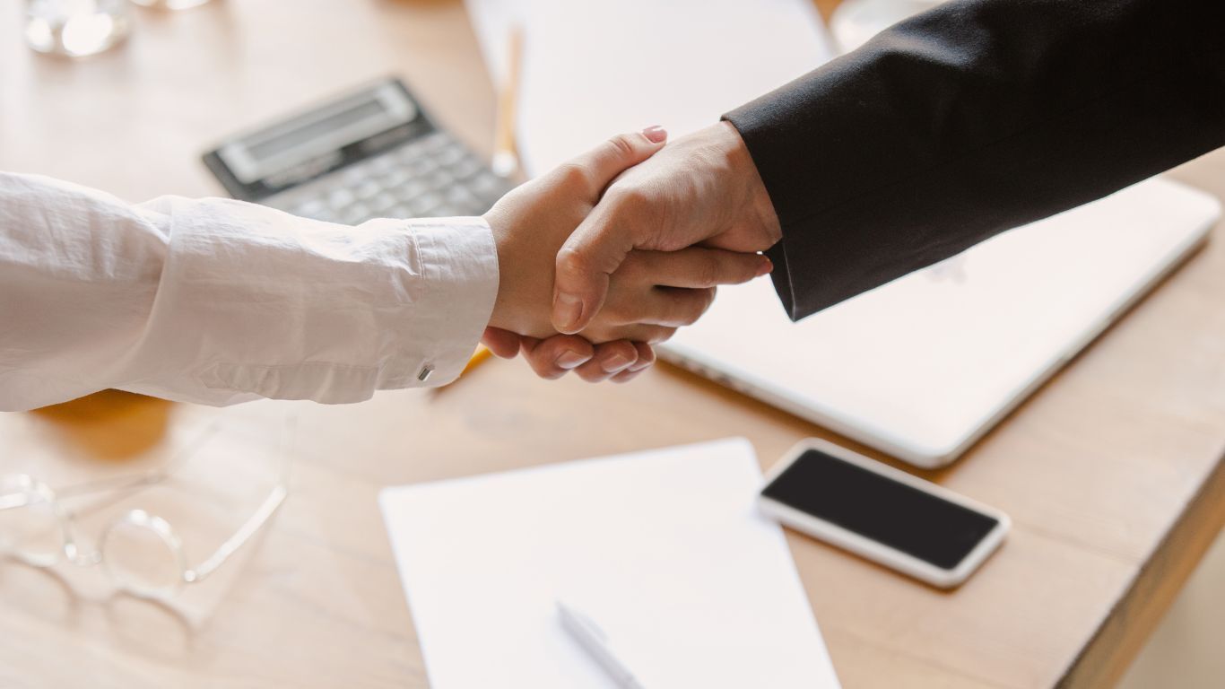 Business handshake over documents and laptop representing a contractor sales process and client agreement.
