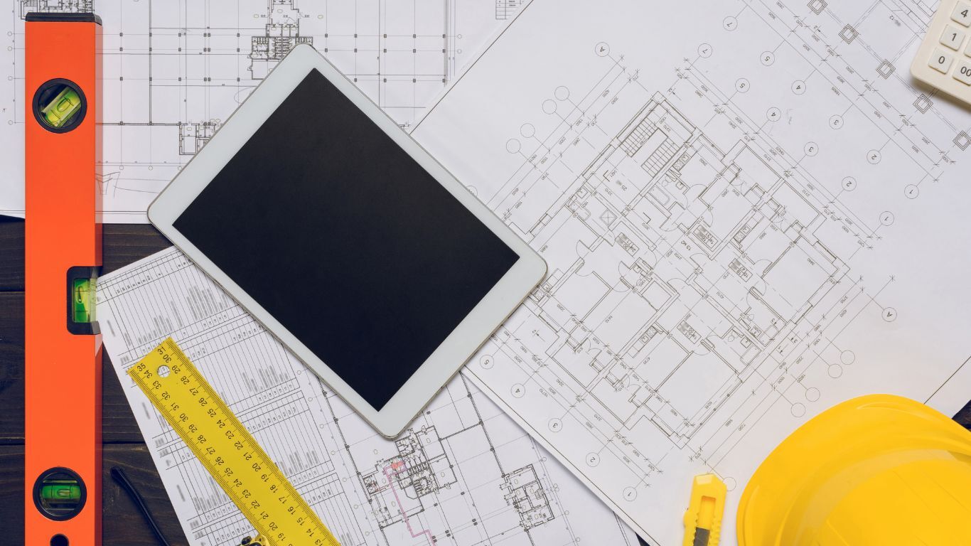 Tablet, blueprints, level, and hard hat representing contractor business management.